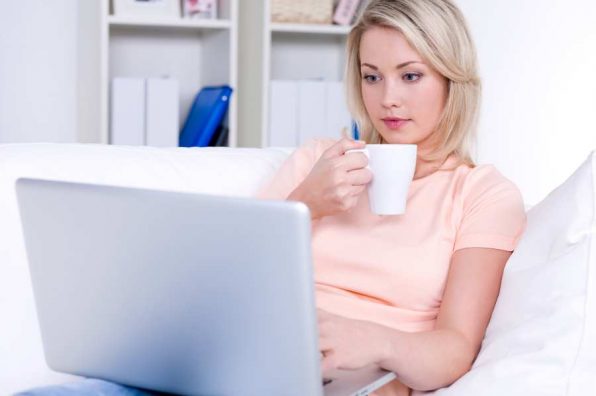 Beautiful young woman drinking coffee and using laptop